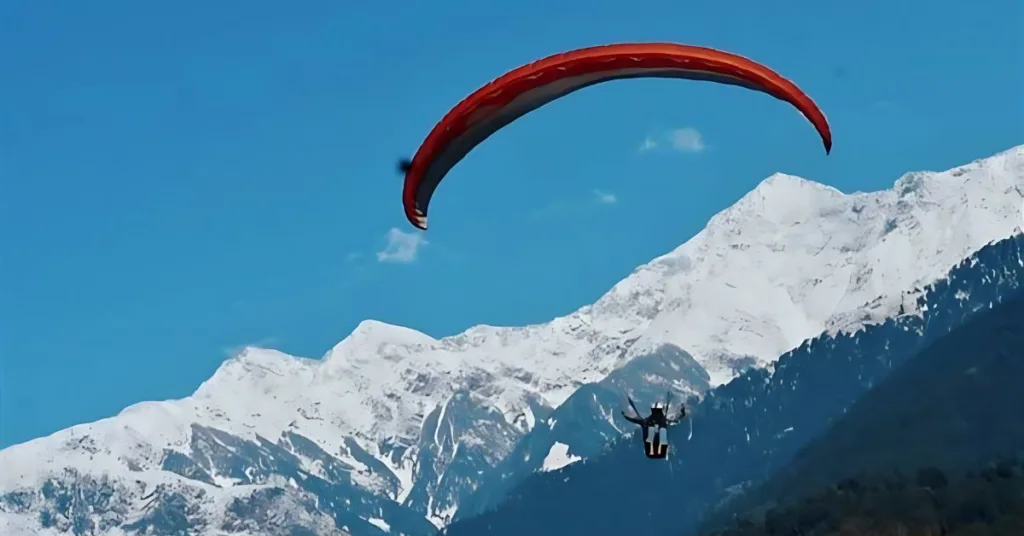 A person paragliding over a snow covered mountain range in Bir Billing